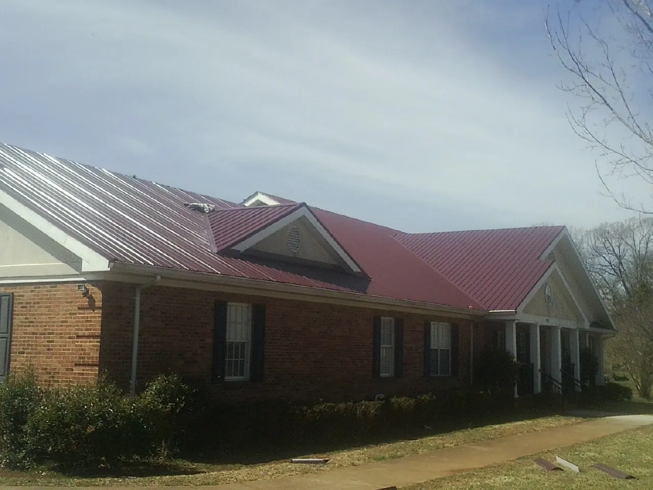 Red metal roof with gabled entries on a long brick building, from a Hail Damage Roof Repair job in Tamaqua