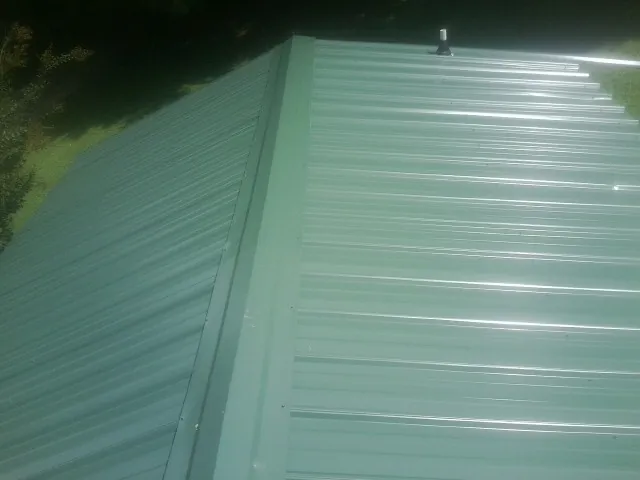 New green metal panels meeting at the ridge of a roof — Flat Roof Repair work by our crew in Tamaqua