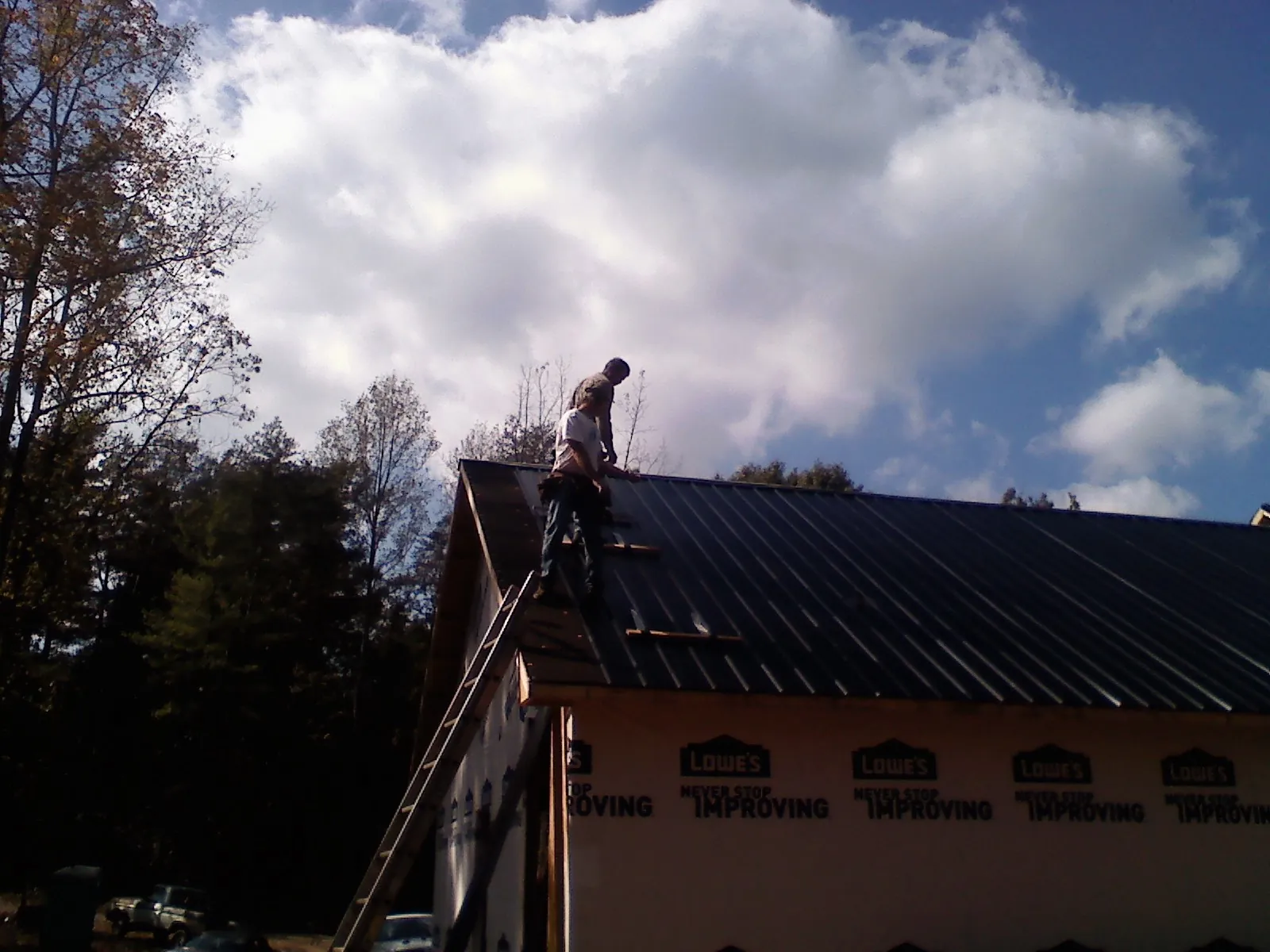 Roofer fastening dark metal panels high against a cloudy sky, from a Roof Inspection job in Tamaqua