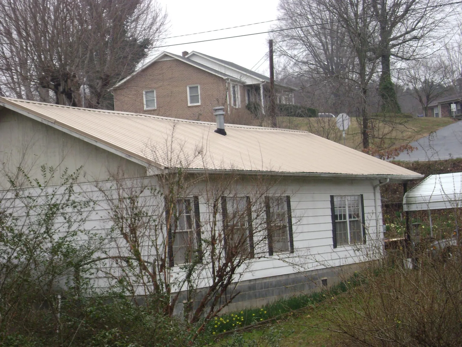 Tan metal roof on a white sided house set into a hillside — Commercial Roofing by Roofing Brothers in Tamaqua